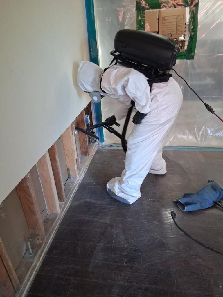 A technician with a backpack vacuum in a hallway with the wall cut and the floor covered