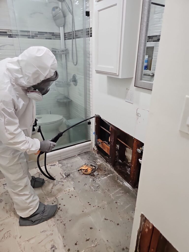 A technician running a hose in a bathroom with a glass shower and the baseboard cut
