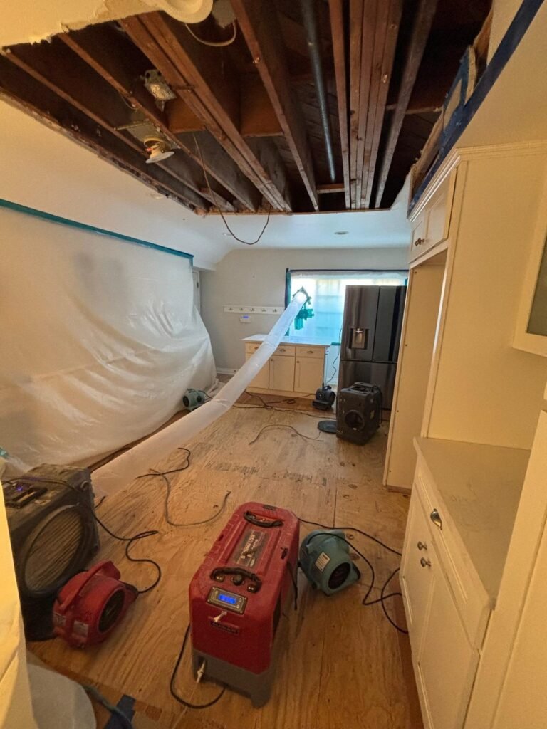 A kitchen with the ceiling opened to the joists, containment up and dehumidifiers running