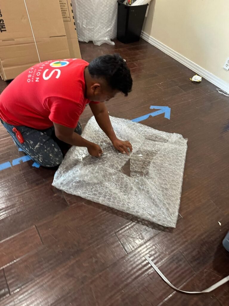 An SOS technician wrapping a framed piece in bubble wrap on the floor in Ventura County