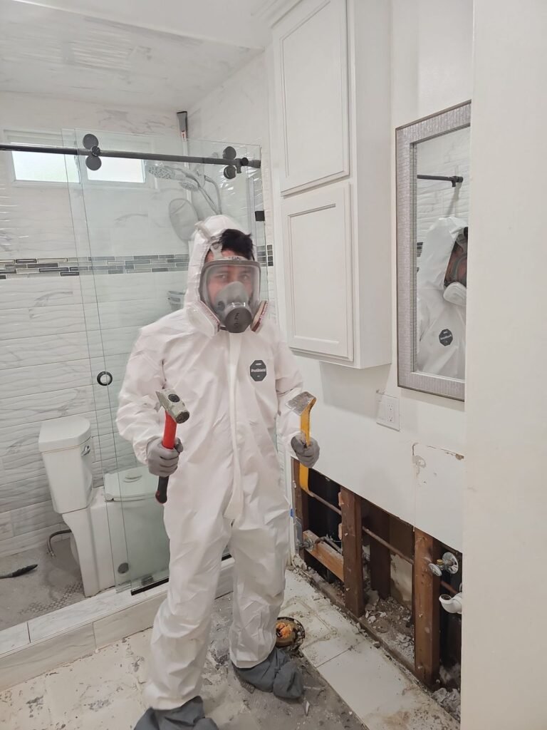A suited technician holding two hammers beside an opened bathroom vanity