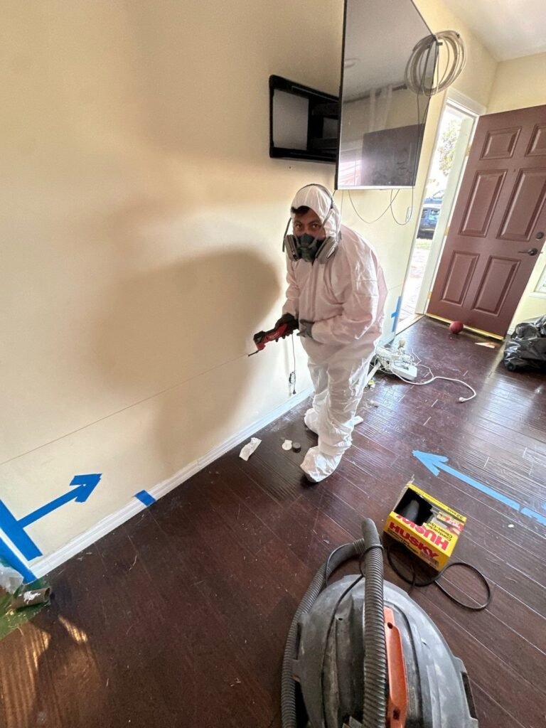 A technician spraying along the baseboard of a room with dark hardwood in Ventura County